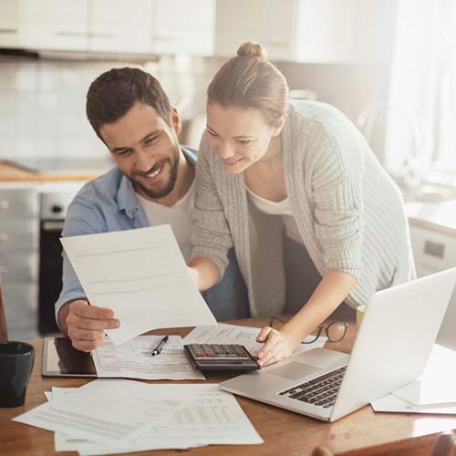 Couple reviewing financial paperwork with a calculator and laptop at home